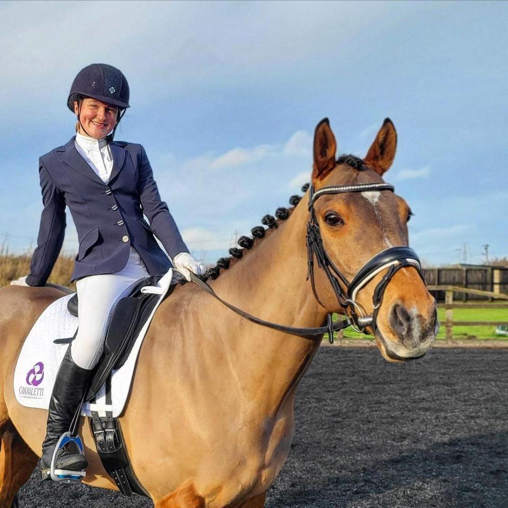 Rider in formal equestrian attire sitting on a light brown horse with a white Cavaletti Collection saddle pad in an outdoor arena. Photo credit: harrys_newchapter.