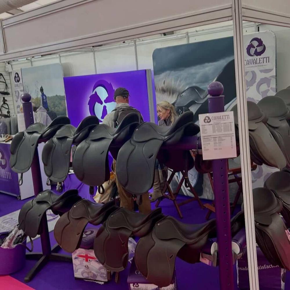 Cavaletti Collection booth at Your Horse Live 2025 displaying multiple black saddles on a purple stand with branded banners and customers browsing the stand