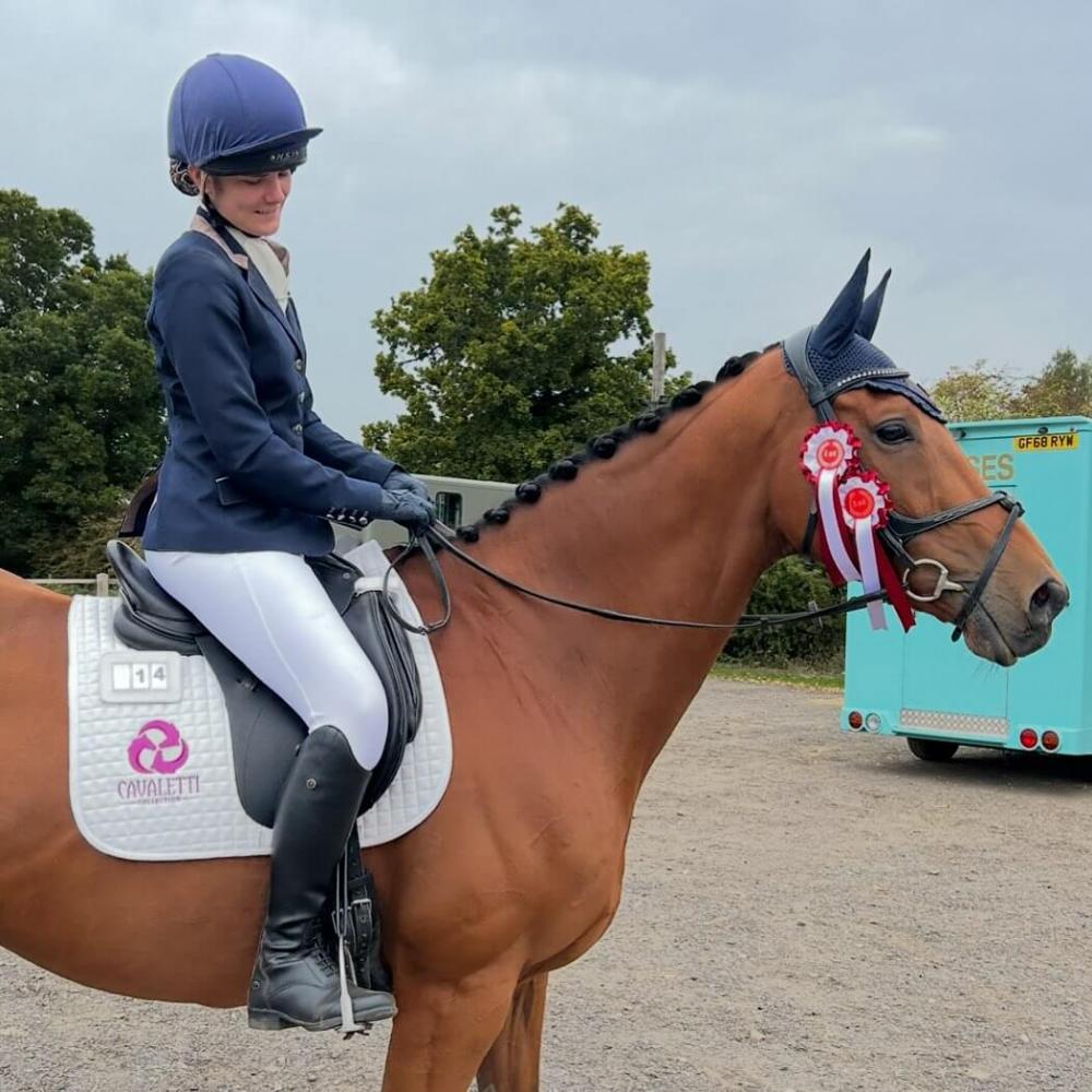 Dressage rider from Team Allerton riding a chestnut horse wearing a Cavaletti saddle pad and bridle, with competition rosettes attached.