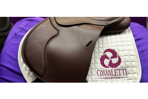 Close‑up of a brown Cavaletti Collection saddle on a white quilted pad with branded embroidery.