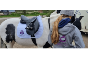Rider standing beside a white‑and‑black horse equipped with a black saddle and white Cavaletti Collection saddle pad in an outdoor setting.
