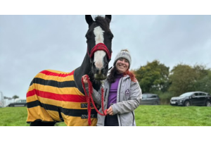 Horse wearing a striped cooler rug standing beside a smiling rider in outdoor autumn weather, showing how to keep horses comfortable in colder temperatures.