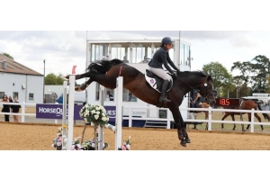 Rider and horse clearing a floral show jump fence in competition