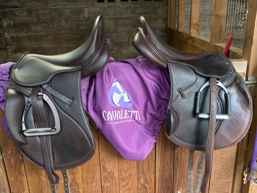 Two Cavaletti Collection saddles on a stable wall with a purple Cavaletti saddle cover in between — highlighting why saddle covers protect and extend the life of your tack.