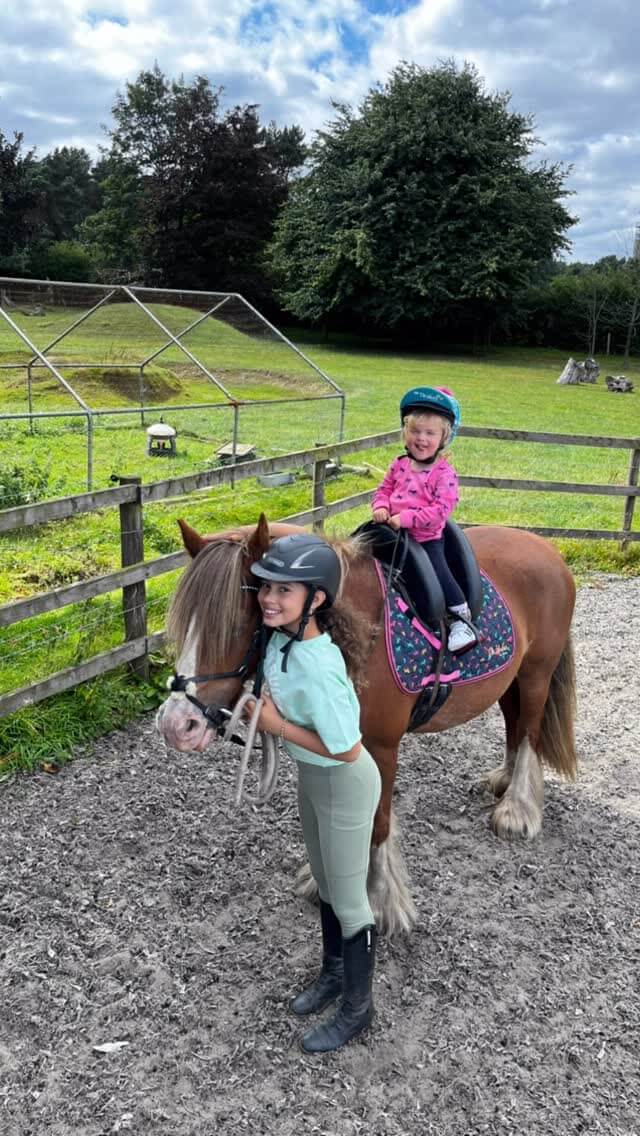 Two children wearing helmets enjoying a pony ride during an equestrian lesson outdoors Cavaletti Collection.