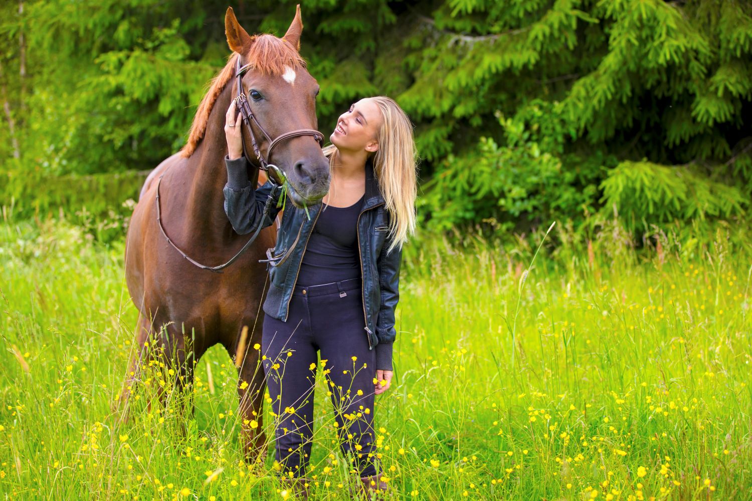 young woman standing in a field with her brown horse
