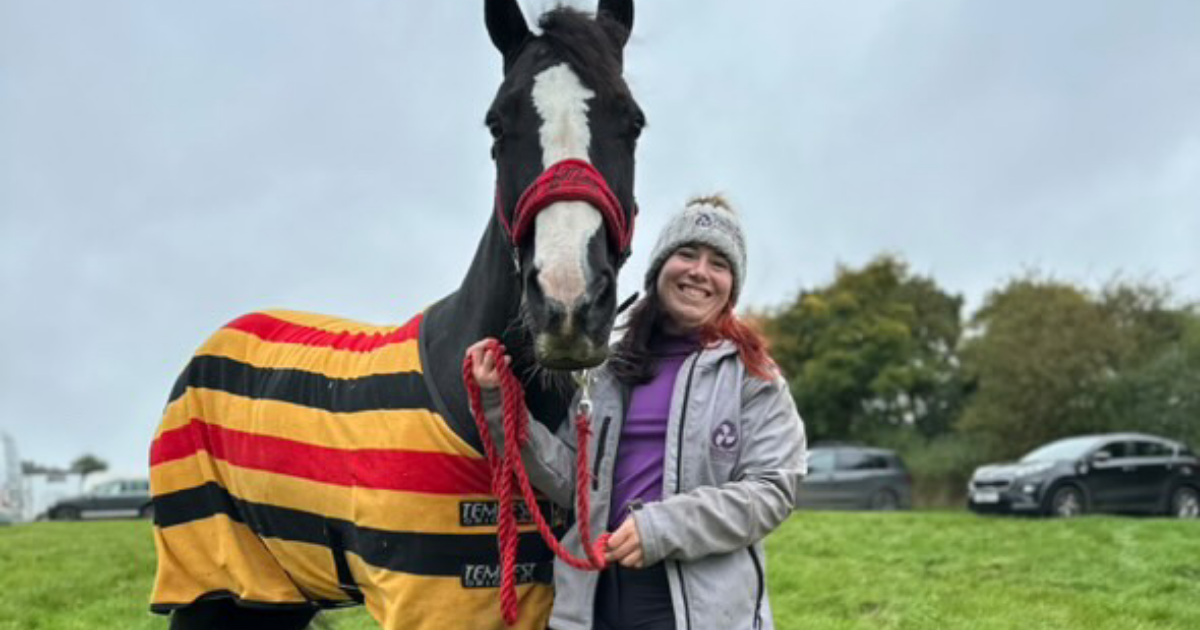 Horse wearing a striped cooler rug standing beside a smiling rider in outdoor autumn weather, showing how to keep horses comfortable in colder temperatures.