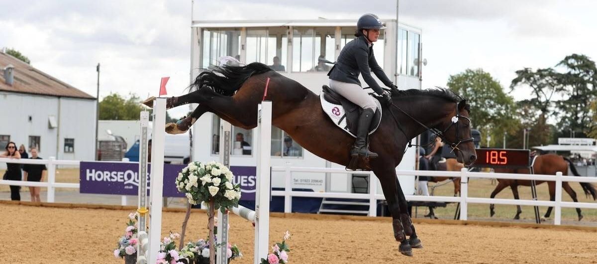 Rider and horse clearing a floral show jump fence in competition